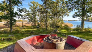 A fire pit with a red border, surrounded by grass and trees, overlooking a body of water.