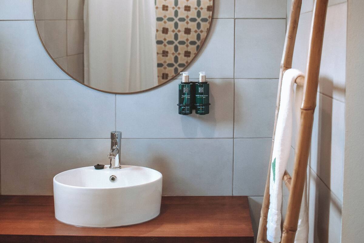 A bathroom with a round mirror, a wooden vanity, a white sink, and a shower curtain with a geometric pattern.