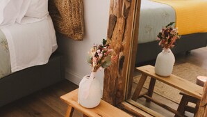 A bedroom with a bed, a bedside table with a vase and candle, a mirror, and a wooden bench.