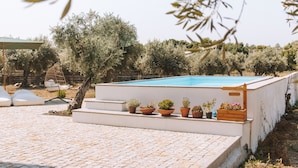 A pool area with steps leading to a white wall, potted plants, and a hanging chair.