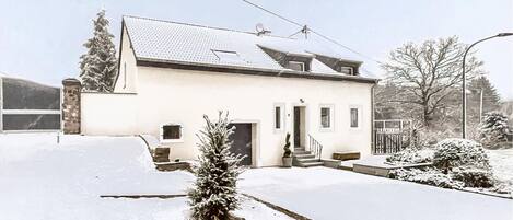 A two-story house with a snow-covered lawn, a small tree, and a visible garage.
