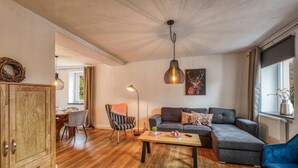 A cozy living room with a wooden cabinet, a sofa, a coffee table, and a chair. There is a window with curtains and a painting on the wall. - Beautiful home in Nimsreuland with WiFi (Nimsreuland)
