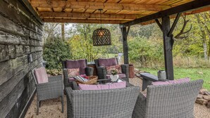 A covered outdoor seating area with wicker furniture and cushions, a hanging light fixture, and a view of the surrounding greenery. - Beautiful home in Nimsreuland with WiFi (Nimsreuland)