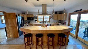 Una cocina moderna con una isla grande, taburetes de bar, lámparas colgantes y vistas a través de la puerta de cristal.