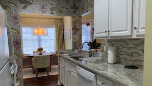 Una cocina compacta con armarios blancos, encimera de granito y lavavajillas integrado.
