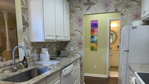 Una cocina con armarios blancos, encimera de granito, pileta de acero inoxidable y refrigerador.