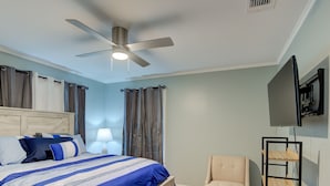 Une chambre à coucher avec un lit, une chaise, un téléviseur et un ventilateur de plafond.