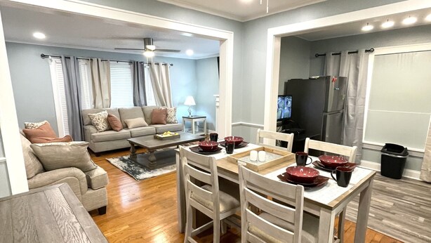 Un salon moderne avec un coin repas, un ventilateur de plafond et une cuisine visible à travers une porte ouverte.