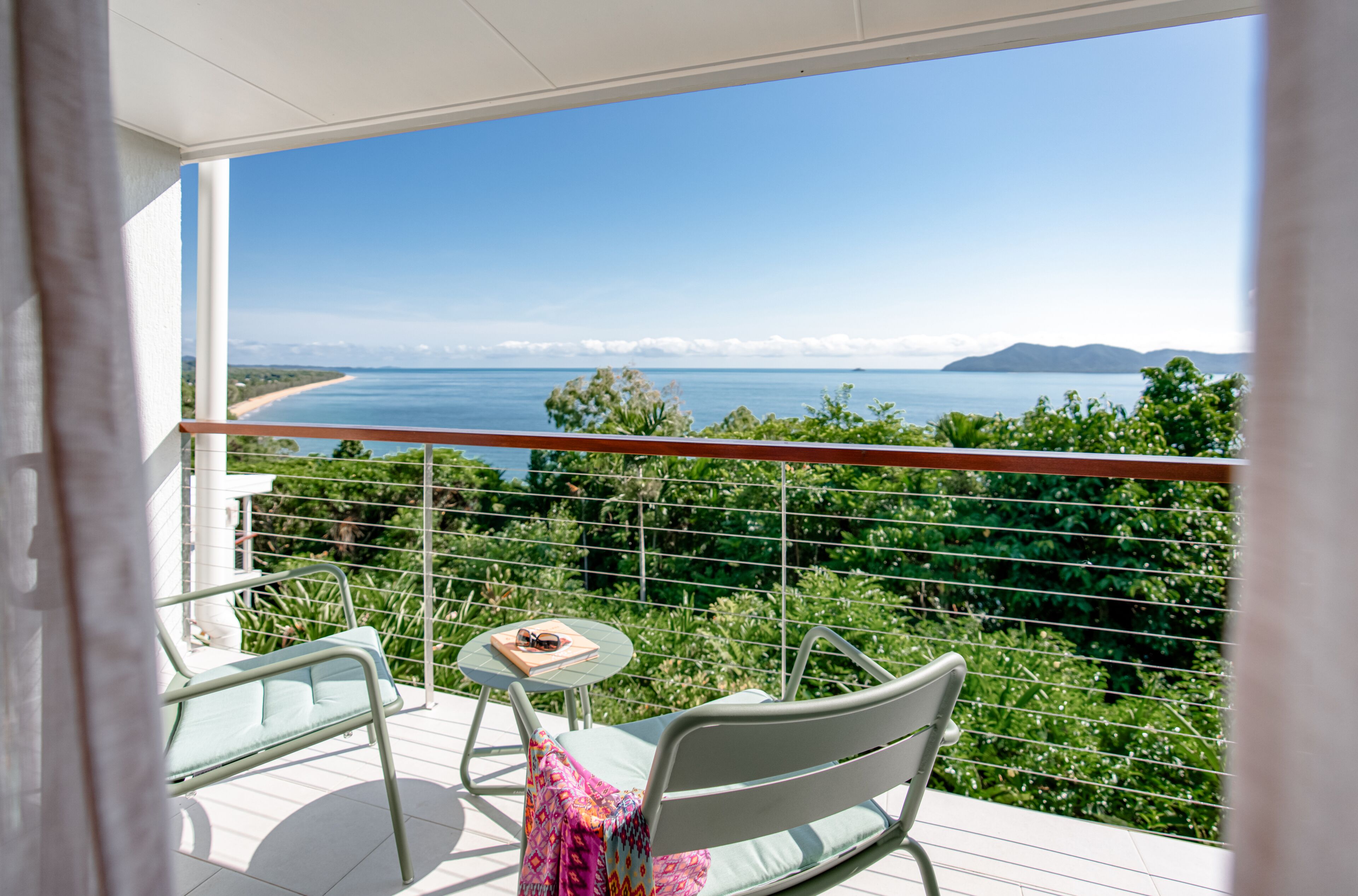 Ein Balkon mit Meerblick, zwei Stühle, ein kleiner Tisch und ein Buch.