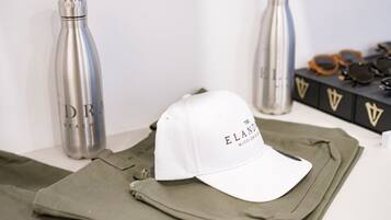 A white cap with "ELAND" text, a green jacket, and two stainless steel bottles on a white surface.