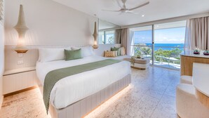 A modern hotel room with a large bed, a balcony with a view of the ocean, and a ceiling fan. - The Elandra (South Mission Beach)