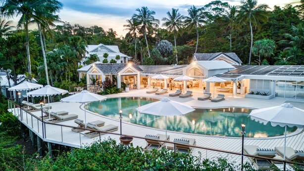 A resort with a large pool, sun loungers, umbrellas, and a well-lit outdoor area surrounded by lush greenery. - The Elandra (South Mission Beach)