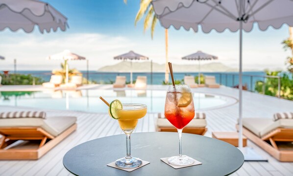 Two drinks on a table by a poolside with lounge chairs and umbrellas in the background. - The Elandra (South Mission Beach)