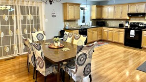 A modern kitchen with wooden cabinets, a dining table with patterned chairs, and a ceiling fan.