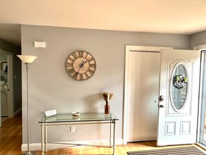 Ein Zimmer mit Glastisch, Wanduhr, Tür mit Willkommensschild und Lampe.
