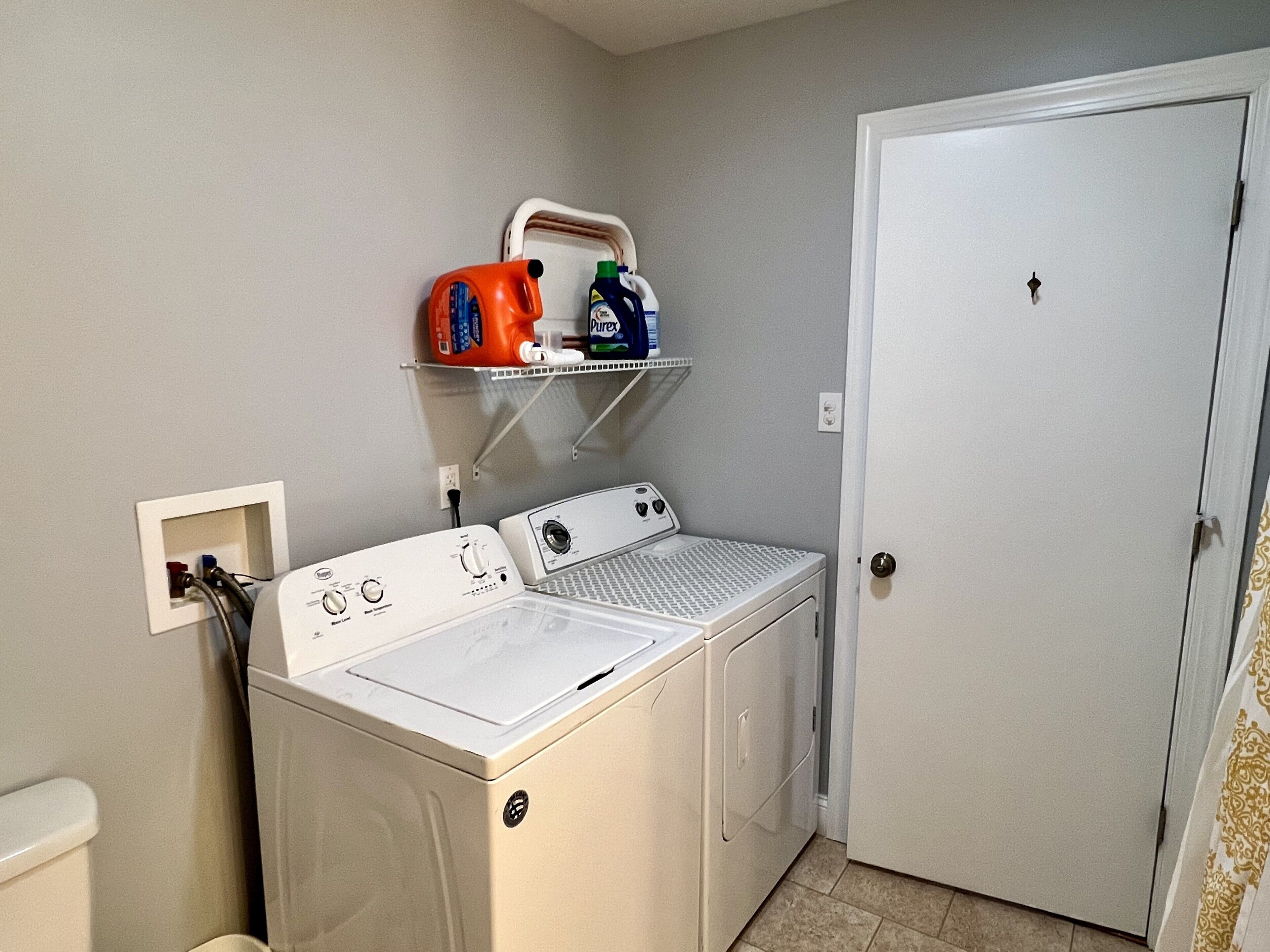 Une buanderie équipée d’un lave-linge et d’un sèche-linge à chargement frontal, d’une étagère pour ranger les produits de lessive et d’une porte.