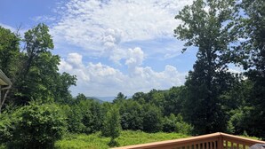 A wooden deck with a view of a forested landscape and distant hills.