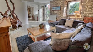 Ein gemütliches Wohnzimmer mit einer Steinwand, einem Holztisch, einem grauen Sofa mit Kissen und einer Vase auf dem Tisch.