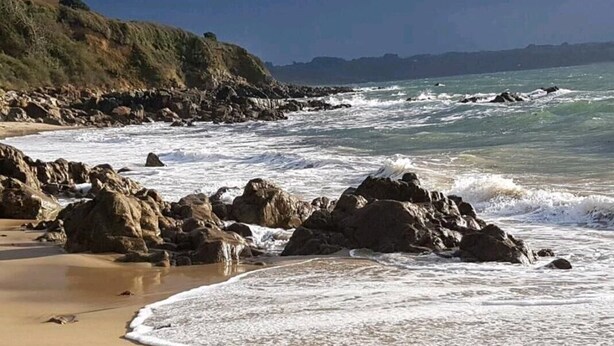 Ein Strand mit felsigem Ufer und brechenden Wellen.