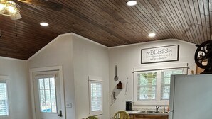 A spacious living area with a wooden ceiling, a dining table with chairs, a blue sofa, and a kitchen in the background. - Casa Azul - Cozy cabin centrally located downtown Bandera (Bandera)