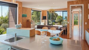 Een moderne keuken met een centraal eiland, een eethoek met tafel en stoelen, en grote ramen met uitzicht op de omgeving.