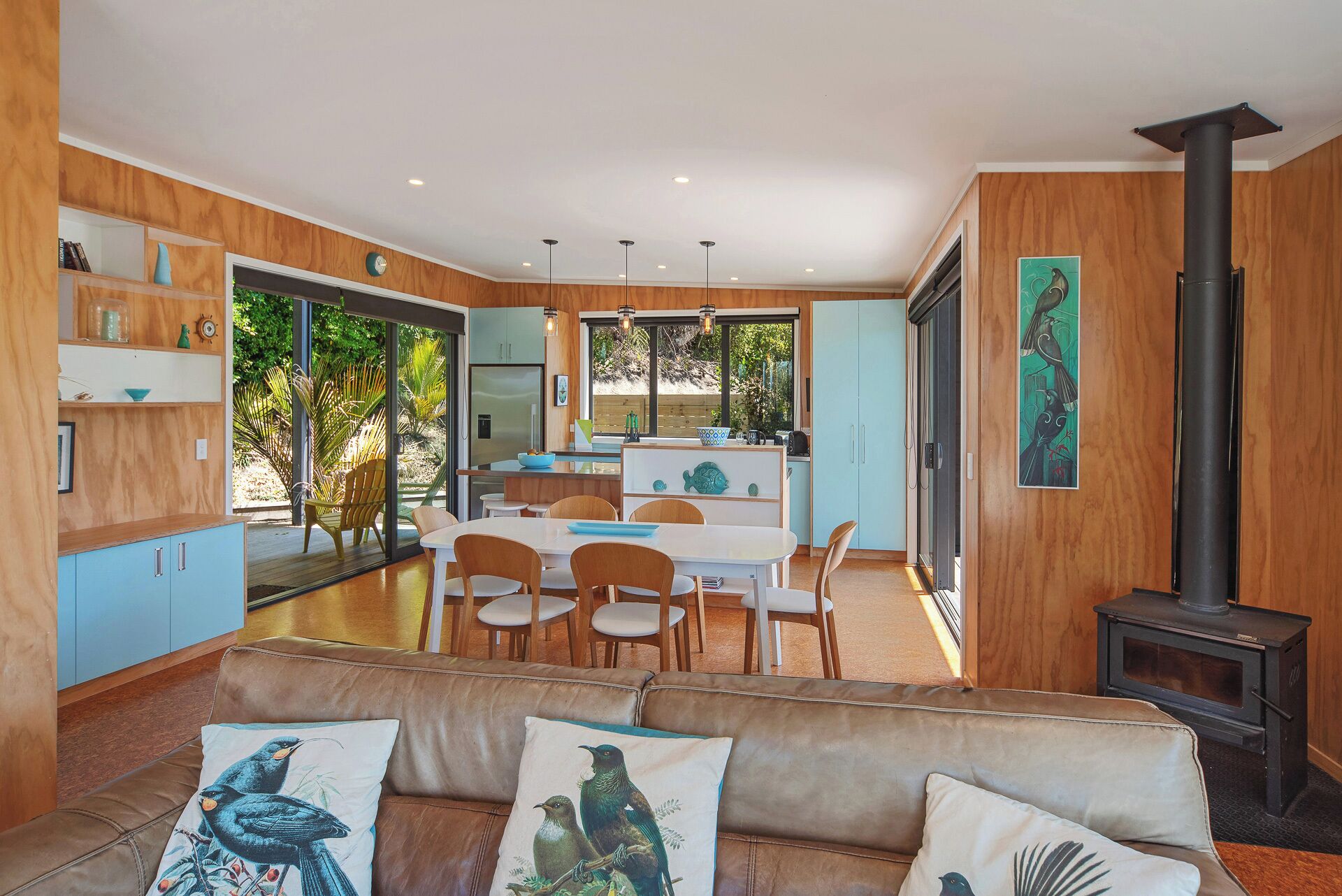 A modern kitchen with a dining area, a sofa with bird-themed cushions, and a wood-burning stove.
