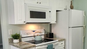 Een keuken met witte kastjes, een magnetron, een fornuis en een koelkast.