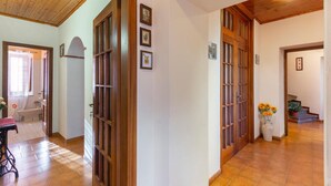 Un pasillo con puertas de madera y suelo de baldosas que conduce a un baño con lavamanos y ducha.