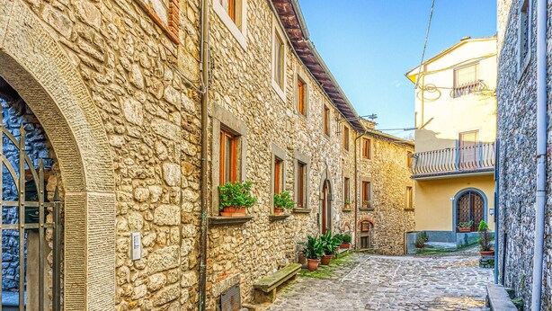 Una estrecha calle adoquinada bordeada por edificios de piedra con puertas y ventanas de arco.