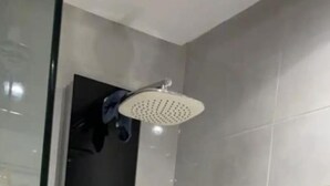 Une douche équipée d’un pommeau de douche à main, d’un panneau de commande fixé au mur et d’une paroi en verre.