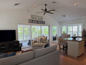 A spacious living area with a large flat-screen TV, a ceiling fan, and a sign indicating 'Palm Island Beach House.'