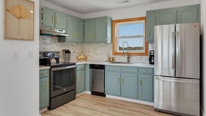 A modern kitchen with teal cabinets, stainless steel appliances, and a window providing a view. - Gorgeous, Ocean View, 3 bedroom, 2 bathroom home in the heart of Kitty Hawk! (Kitty Hawk)