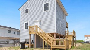 A two-story house with a wooden deck and a staircase leading to the front door. - Gorgeous, Ocean View, 3 bedroom, 2 bathroom home in the heart of Kitty Hawk! (Kitty Hawk)