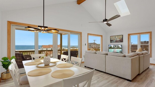 A spacious living area with a large sofa, dining table with placemats, and a ceiling fan. - Gorgeous, Ocean View, 3 bedroom, 2 bathroom home in the heart of Kitty Hawk! (Kitty Hawk)