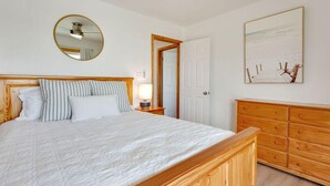 A bedroom with a wooden bed, a bedside table with a lamp, a mirror, a wooden dresser, and a framed picture on the wall. - Gorgeous, Ocean View, 3 bedroom, 2 bathroom home in the heart of Kitty Hawk! (Kitty Hawk)