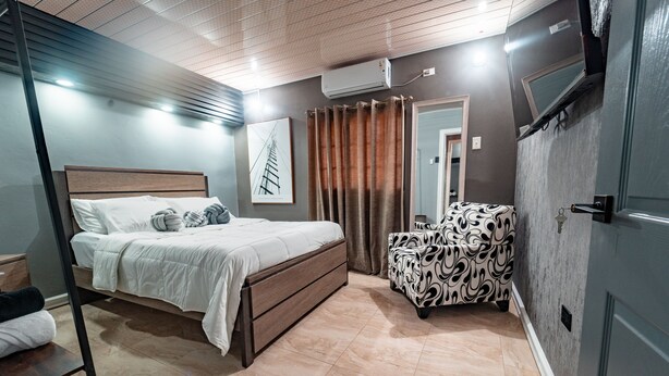Un dormitorio con cama, una silla, un espejo y un equipo de aire acondicionado.