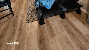 Una sala de estar con un sofá negro, un televisor montado en la pared y piso de madera.