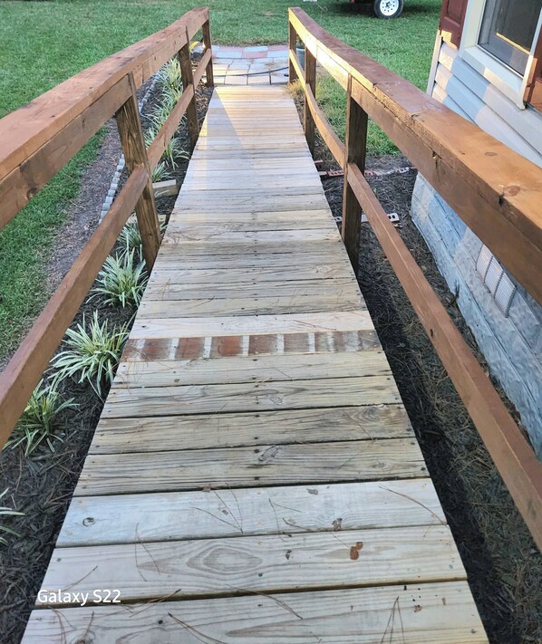 Um deck de madeira com guarda-corpo que leva a uma casa.
