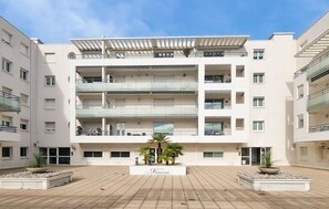 A multi-story residential building with balconies, a central courtyard with palm trees, and a sign reading "Residence La Palmeraie".
