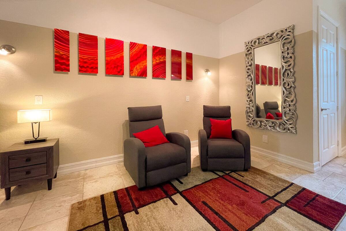 Una habitación con dos sillones, una alfombra, una lámpara, un espejo y varias obras de arte rojas en la pared.