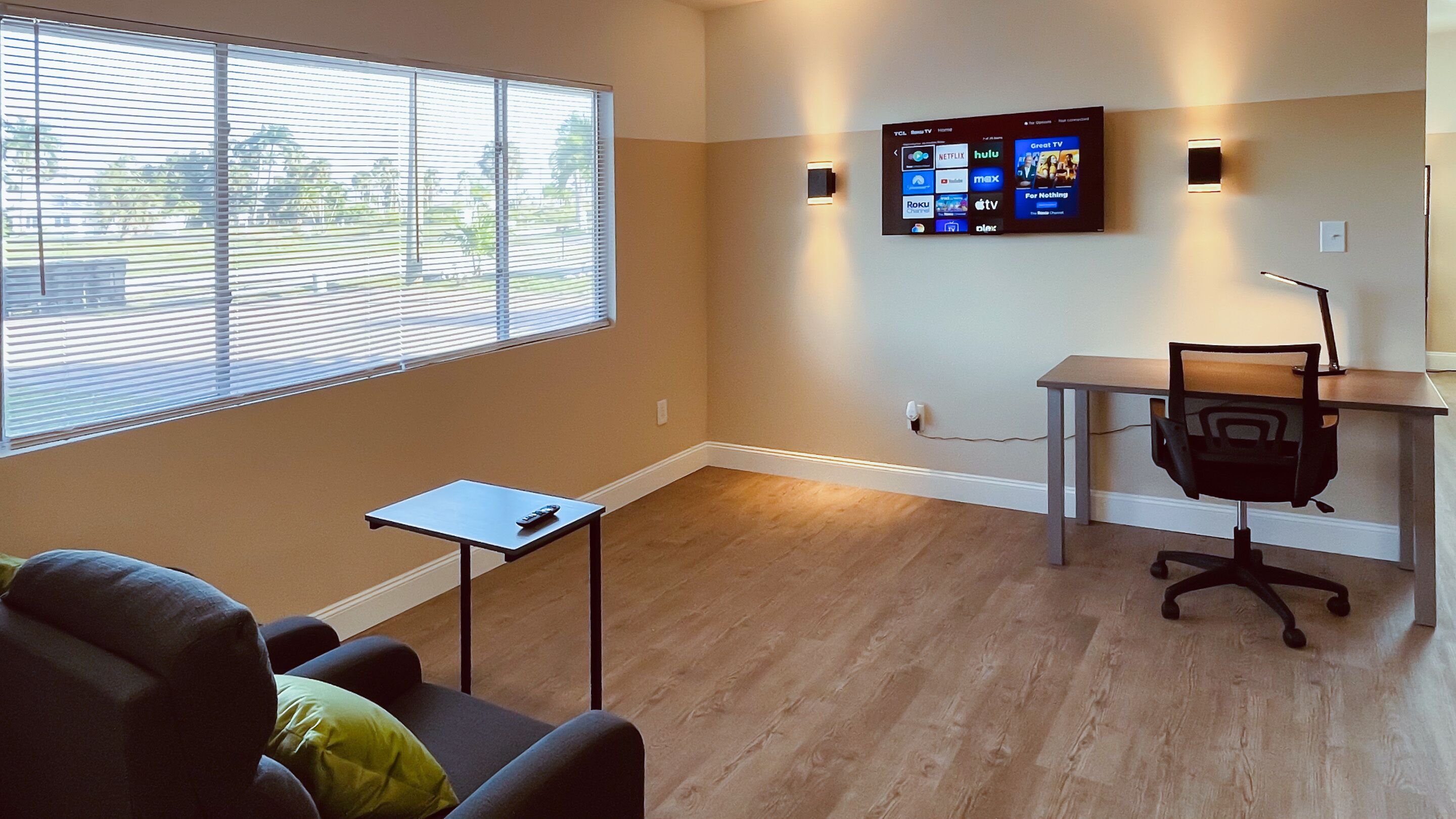 Un espace de bureau moderne doté d’une grande fenêtre, d’un bureau, d’une chaise et d’un téléviseur fixé au mur, diffusant des services de streaming.