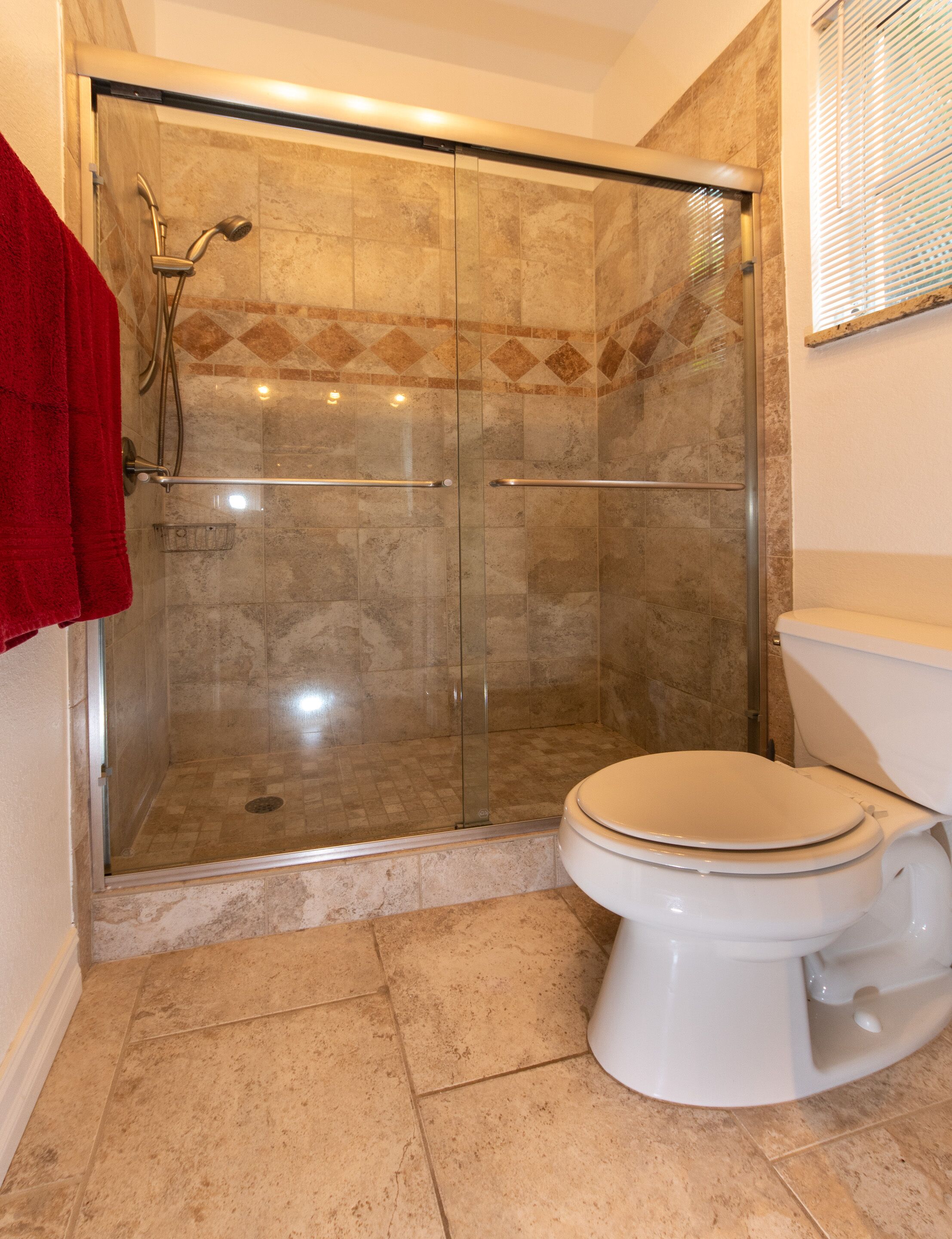 Une salle de bain avec une douche à parois de verre, des toilettes et une serviette rouge accrochée au mur.