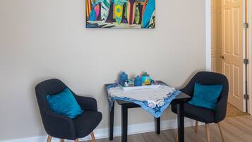 A room with two black chairs, a small table with a blue tablecloth, and a colorful painting on the wall.