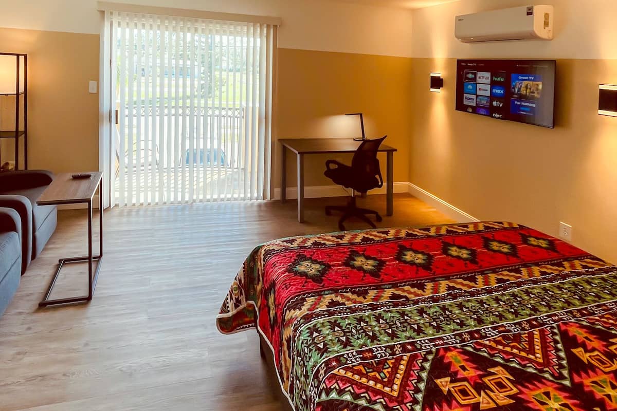 Habitación de hotel con cama, escritorio, silla, sofá y ventana con persianas.