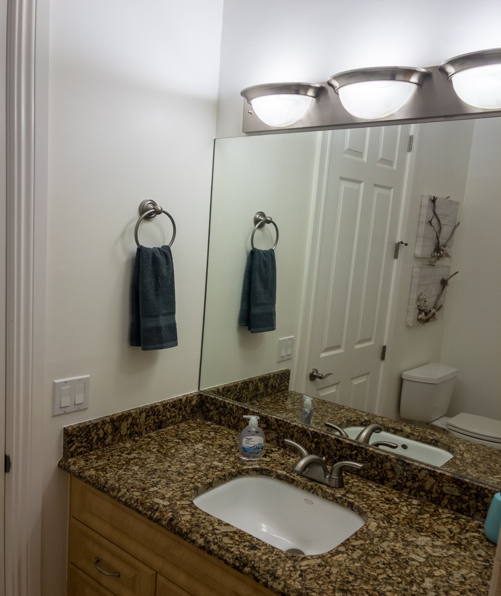 Une salle de bain avec un comptoir en granit, un lavabo, un miroir et deux serviettes suspendues à des porte-serviettes.