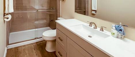 Une salle de bain moderne avec une douche à parois de verre, des toilettes blanches et un meuble-lavabo avec un évier et un miroir.