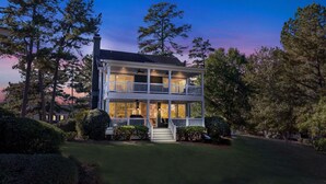 A two-story house with a balcony on the upper floor, surrounded by trees and a well-maintained lawn.