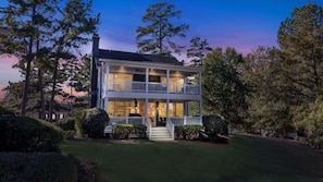A two-story house with a balcony on the upper floor, surrounded by trees and a well-maintained lawn.