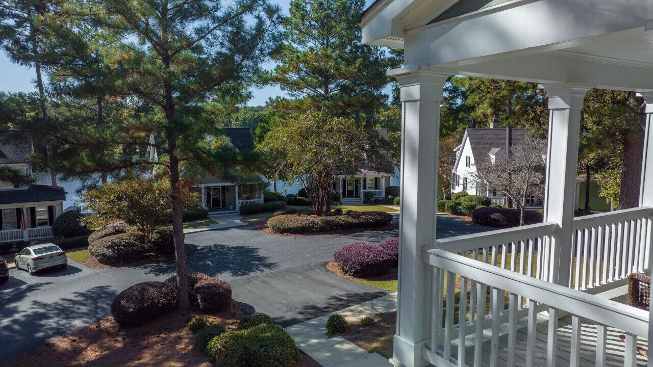 A residential area with a driveway, a white fence, and houses with gabled roofs.