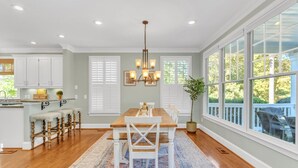 A spacious kitchen with a wooden table, white bar stools, and a chandelier.